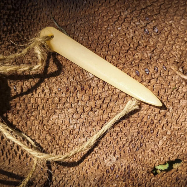 Close-up of a hand-carved bone awl tied with natural cordage, resting on a piece of tanned fish skin.