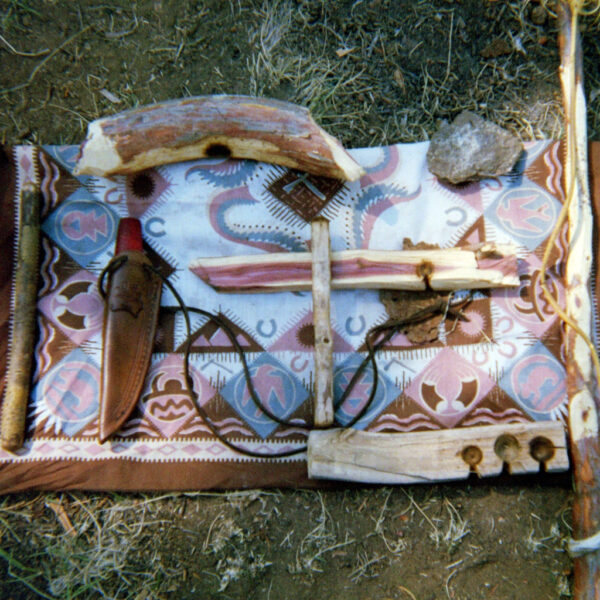 Primitive fire-starting tools laid on a patterned blanket, including a bow drill set, spindle, and handhold.