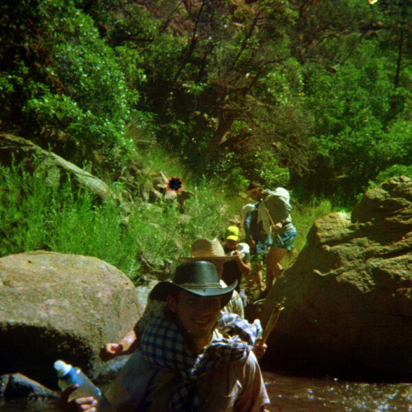 Group crossing rocky creek during primitive wilderness trek, surrounded by steep terrain and dense greenery.