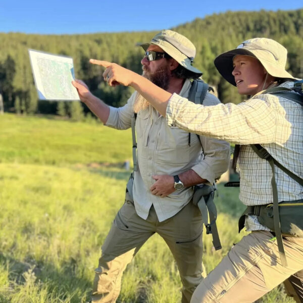 Two people in sun hats examine a map and point across a sunlit field during a navigation exercise.