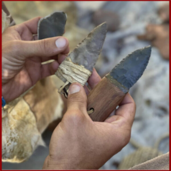 A close-up of hands holding three handmade flint blades, each mounted on different natural handles using sinew or plant cordage, showcasing primitive tool craftsmanship.