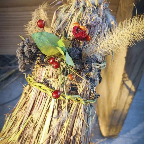 Close-up of a handmade natural broom decorated with wildflowers, berries, and woven grasses, crafted during a wilderness living skills course.