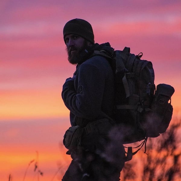 Jason Marsteiner silhouetted against a vibrant sunset, wearing a beanie and carrying a rugged backpack. The scene captures the essence of outdoor adventure and self-reliance.