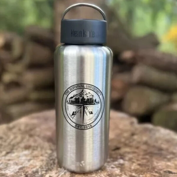 Stainless steel Klean Kanteen bottle with The Survival University logo, sitting on a tree stump in the woods