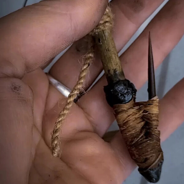 Close-up of a handmade primitive fishing gorge hook, wrapped in natural cordage and held in a weathered hand.
