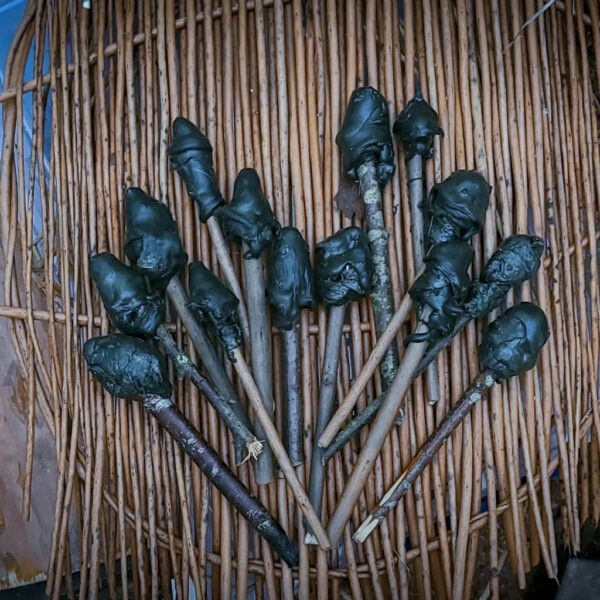 A fan-shaped display of primitive pitch sticks, each tip coated in black resin, laid out on a woven mat made of thin wooden rods.