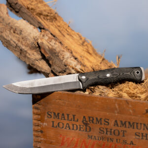 The Courage knife displayed on an old Winchester ammunition crate with wood shavings and antler nearby