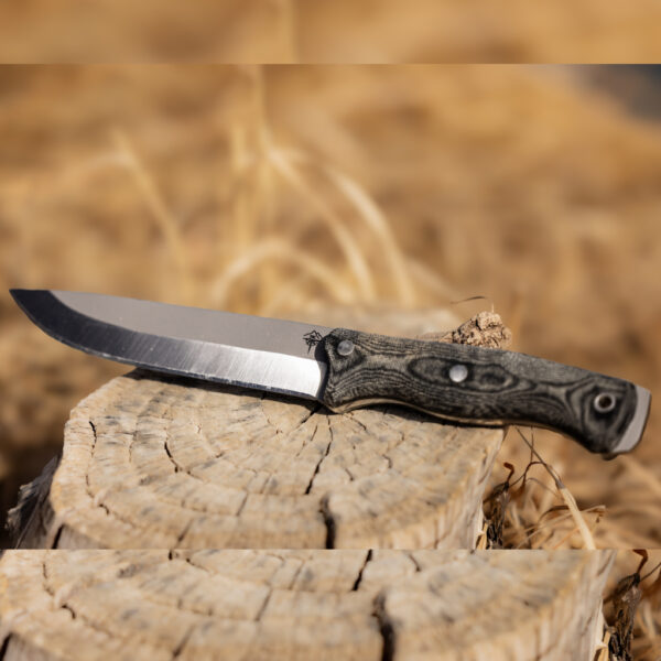 The Courage knife resting on a weathered tree stump with dry grass in the background